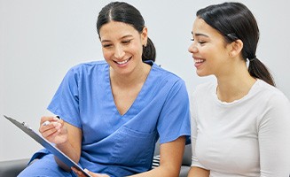 Dental assistant and patient smiling while reviewing paperwork