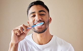 Man smiling while brushing his teeth