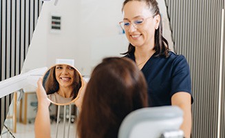 Patient smiling at reflection in mirror next to dental assistant