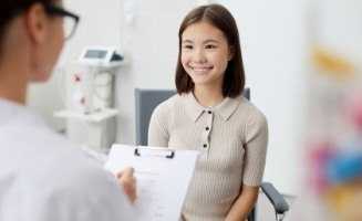 Woman smiling while her dentist writes on clipboard