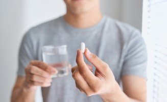 Person holding a pill and a glass of water