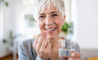 Senior woman holding pill and glass of water