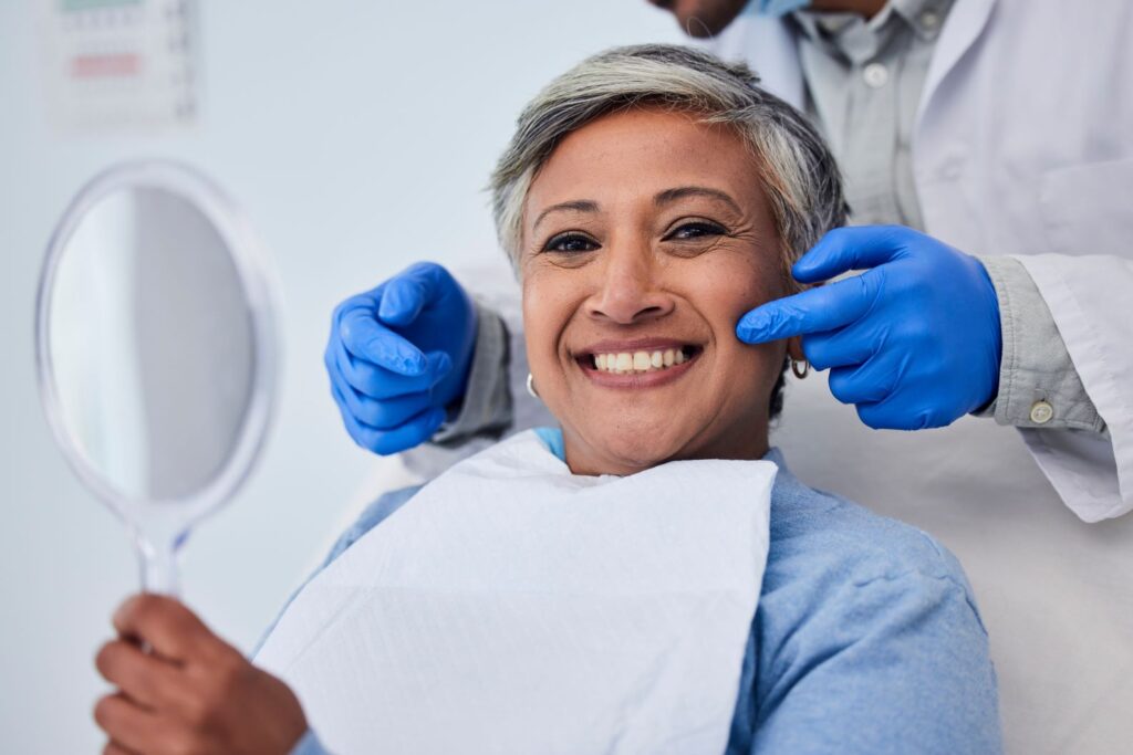 A woman smiling and looking in the mirror at her dentist's office.